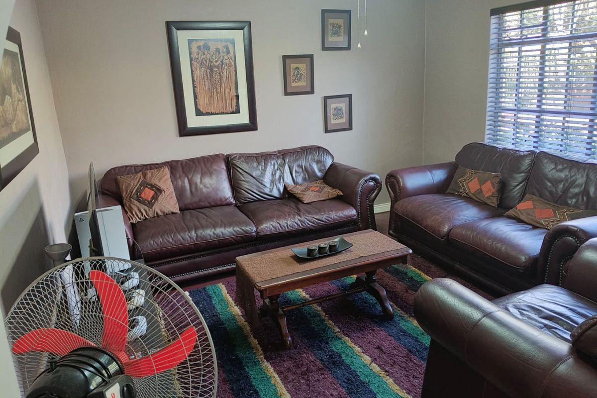 A comfortable living room featuring neutral wall tones, venetian blinds, and a ceiling fan, providing a functional and inviting space for relaxation.