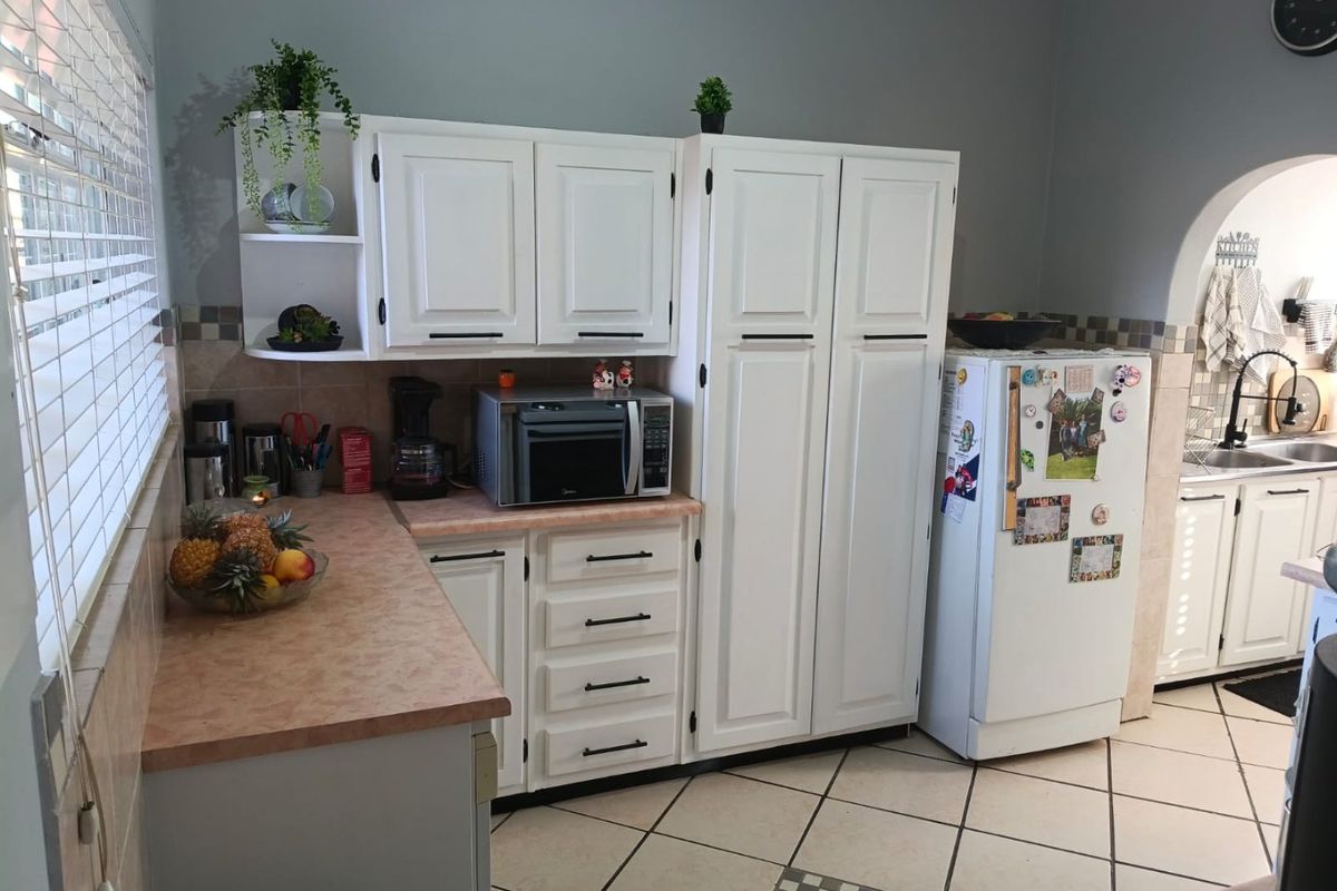 A functional kitchen featuring white cabinetry, laminate countertops, tiled backsplash, and tiled flooring, with an arched opening leading to the sink area.