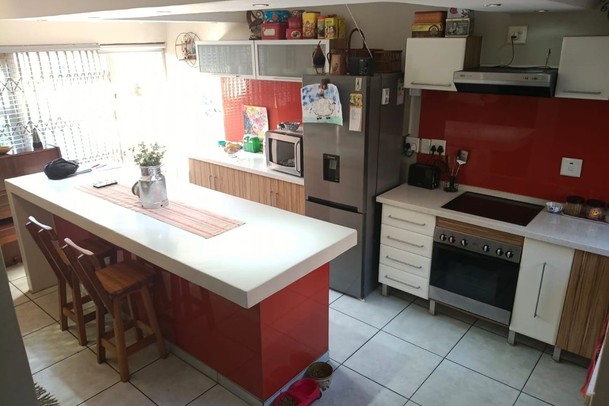 Modern kitchen featuring a central island, built-in oven with electric hob, extractor fan, and vibrant red glass splashbacks with ample storage cabinetry.
