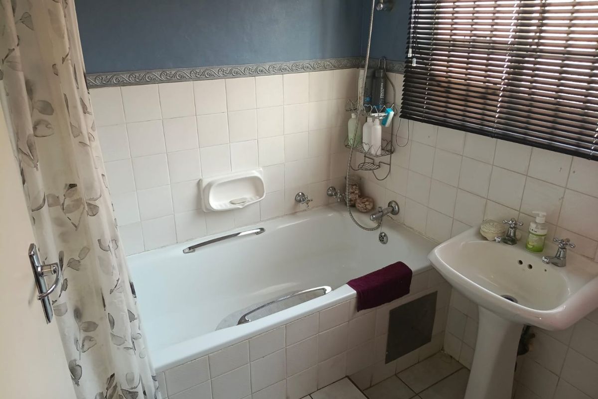 A functional bathroom featuring a built-in bathtub with shower mixer, pedestal basin, and tiled finishes, offering a practical layout for renovation.