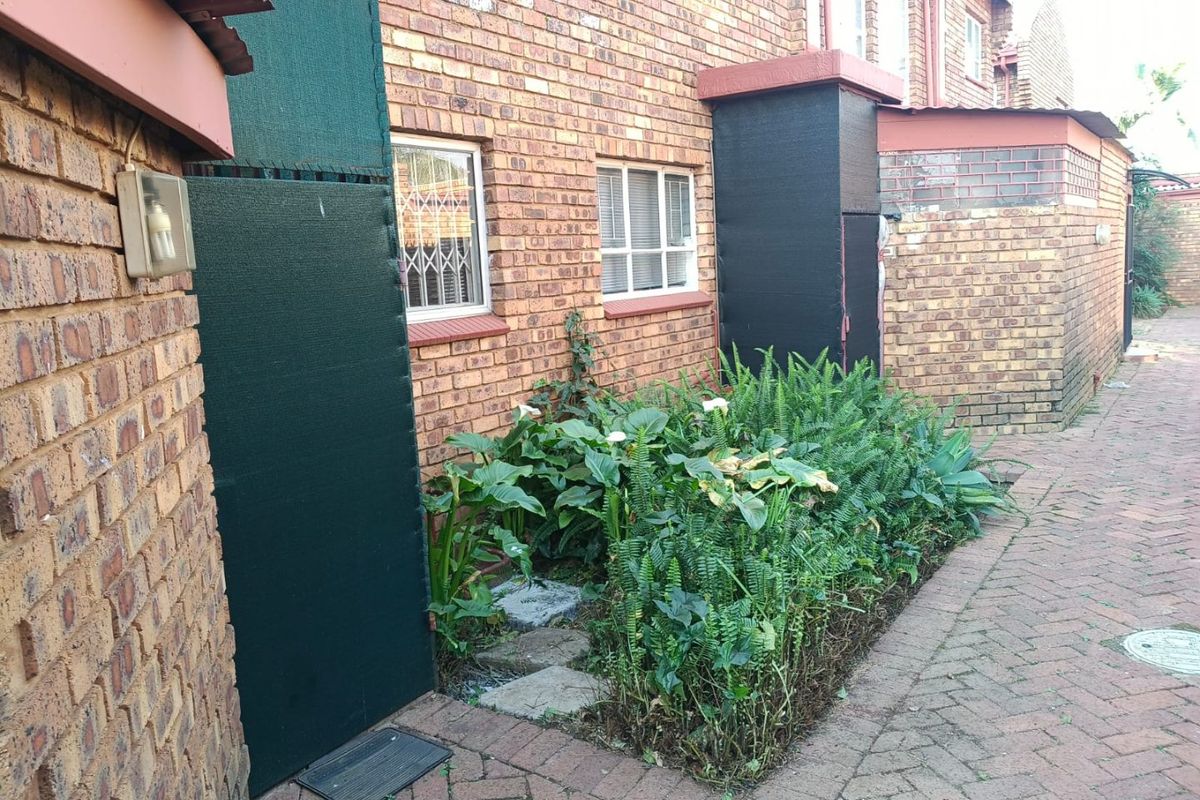 A view of the rear exterior of the townhouse featuring brick walls, security-fitted windows, and a paved walkway alongside a garden bed.