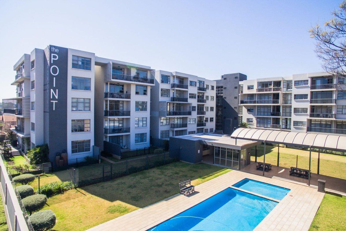 Aerial view of the apartment complex featuring a swimming pool, covered outdoor area, landscaped gardens, and multi-story residential blocks with private balconies.