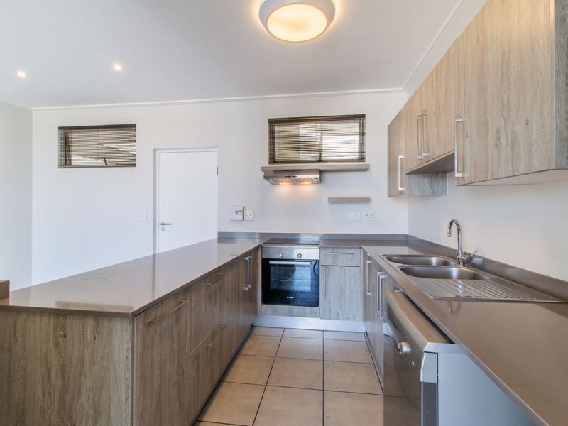 Modern kitchen featuring wood-finish cabinetry, stone countertops, built-in oven, extractor fan, and double sink with tiled flooring.