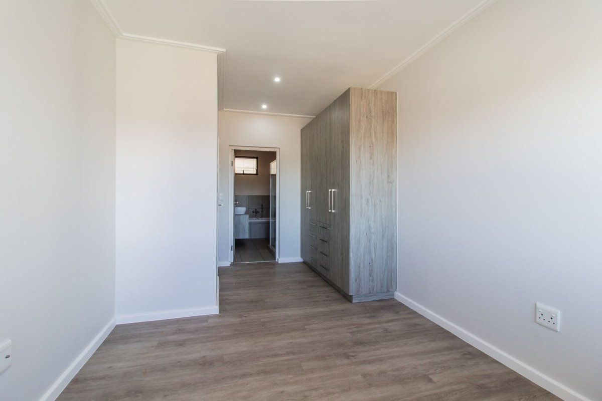 A bright, modern bedroom featuring neutral walls, durable laminate flooring, and ample built-in cupboard space, with direct access to an adjoining bathroom.
