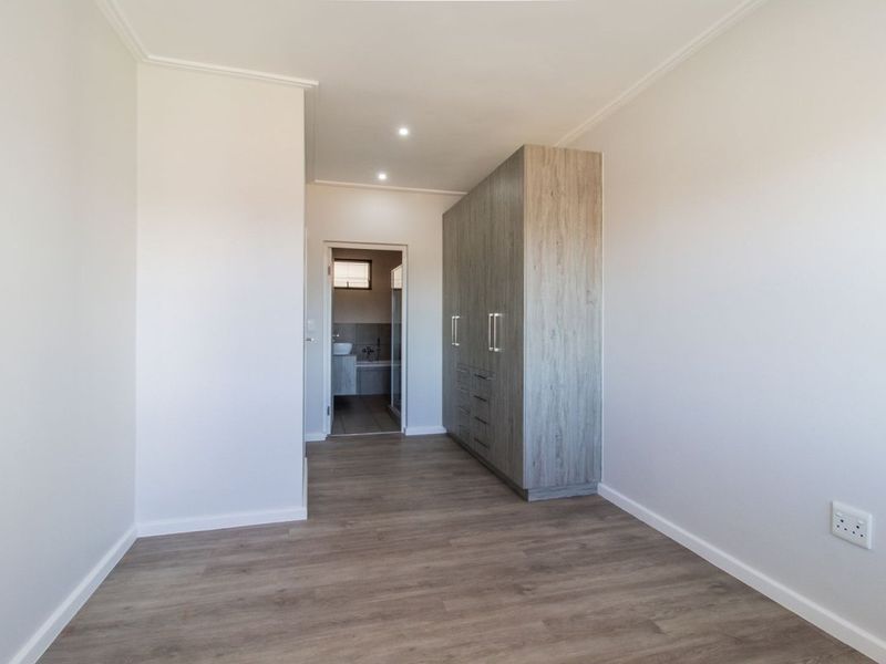 A bright, modern bedroom featuring neutral walls, durable laminate flooring, and ample built-in cupboard space, with direct access to an adjoining bathroom.