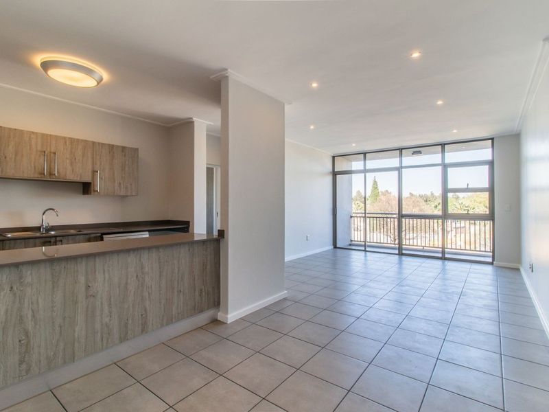 Spacious open-plan living area featuring a modern kitchen with wood-finish cabinetry, tiled floors, and large sliding doors leading to a balcony with scenic views.