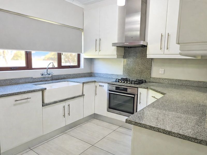 Modern kitchen featuring granite countertops, a farmhouse sink, built-in oven, gas hob, and stainless steel extractor fan with neutral tiled flooring.