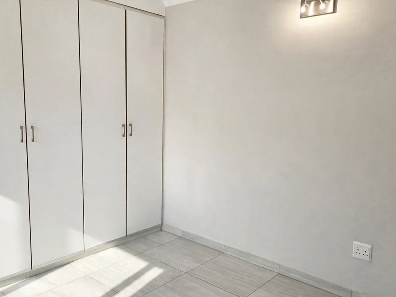 A clean, empty bedroom featuring neutral tiled flooring and ample built-in cupboard storage, ready for personalization.