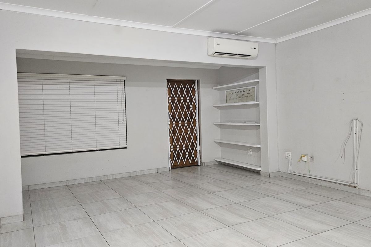 An empty living area featuring tiled flooring, built-in shelving, an air conditioning unit, and a security gate on the door.