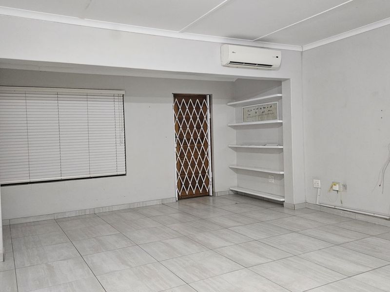 An empty living area featuring tiled flooring, built-in shelving, an air conditioning unit, and a security gate on the door.