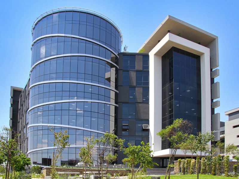 Modern commercial office building featuring a prominent cylindrical glass facade and contemporary architectural design with landscaped surroundings.