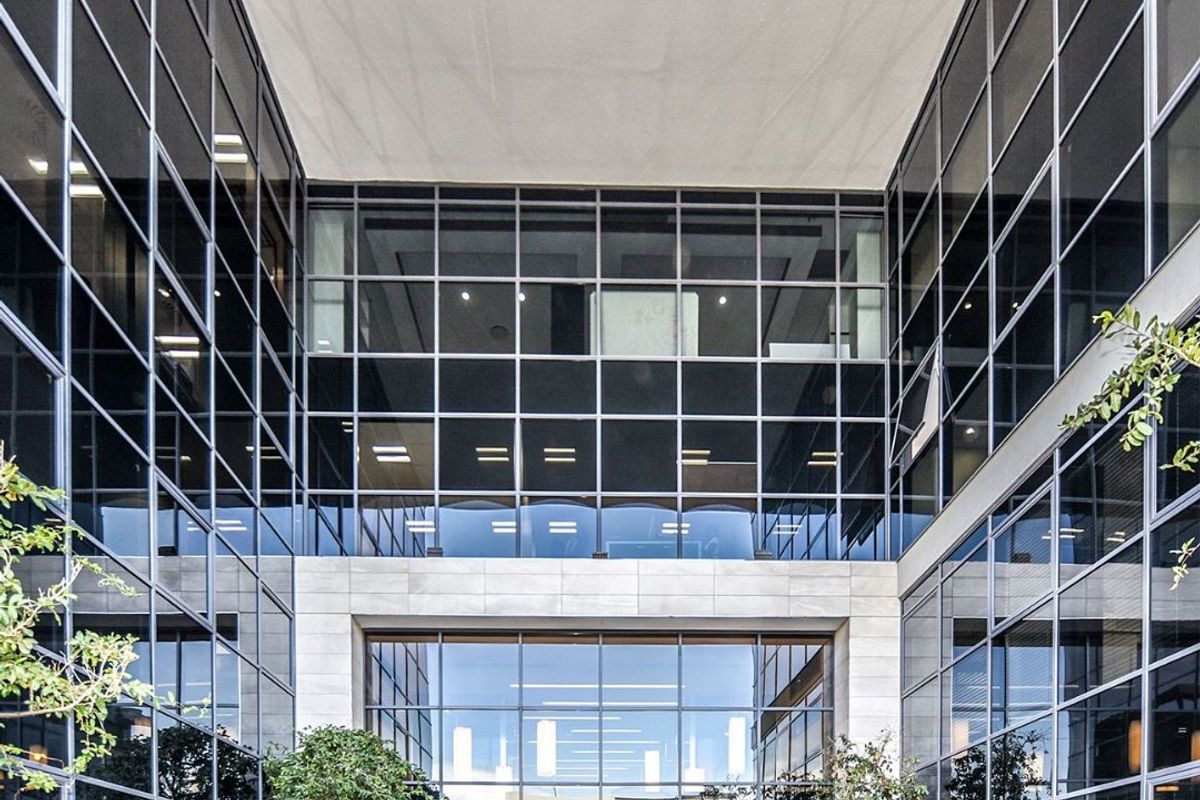 Modern commercial building entrance featuring a striking glass curtain wall facade, stone cladding, and integrated planters leading to a professional lobby area.