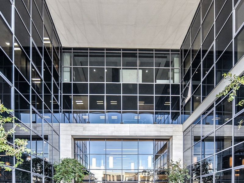 Modern commercial building entrance featuring a striking glass curtain wall facade, stone cladding, and integrated planters leading to a professional lobby area.