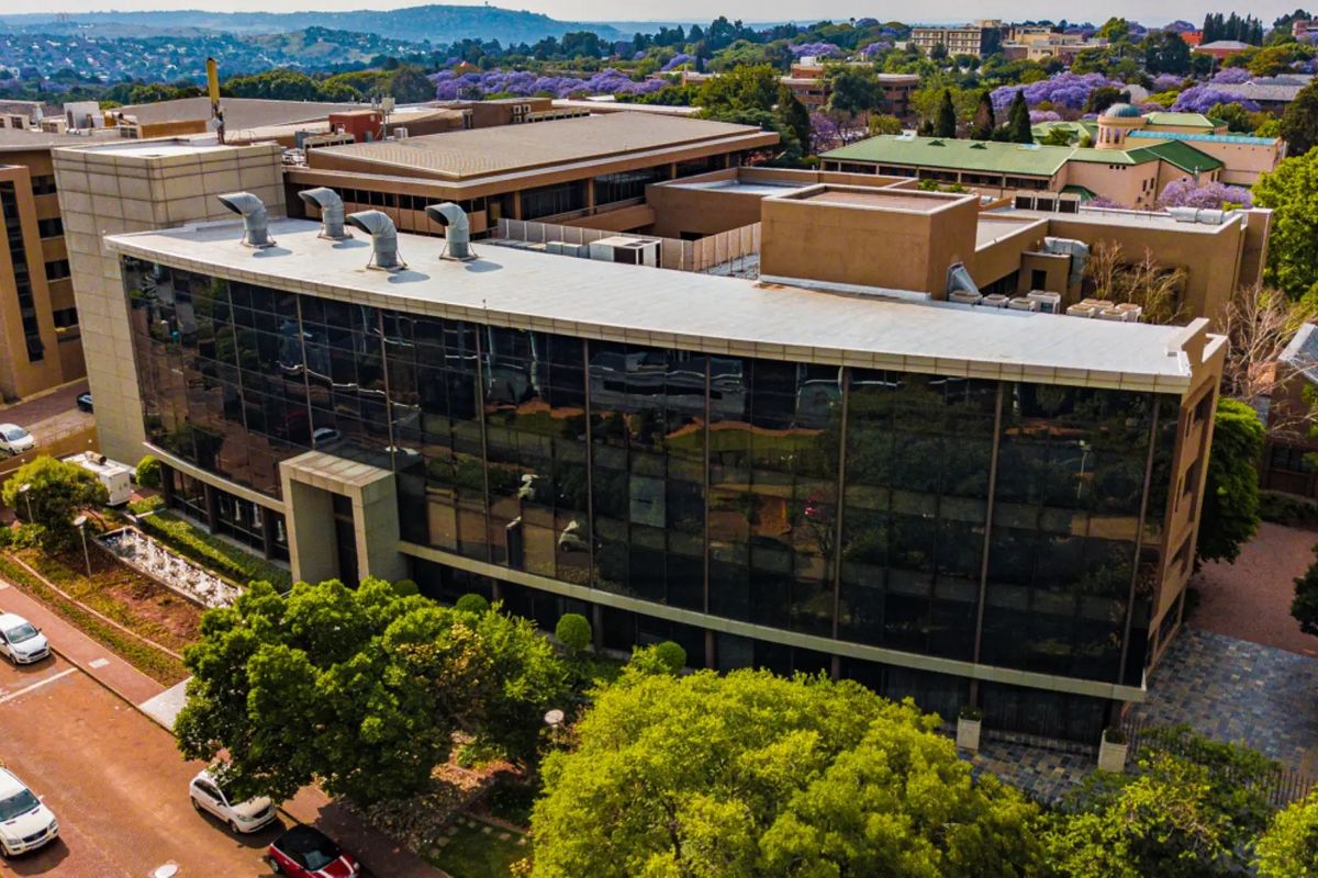 Aerial view of a modern commercial office building featuring extensive glass curtain walling, flat roof infrastructure, and surrounding landscaped grounds.