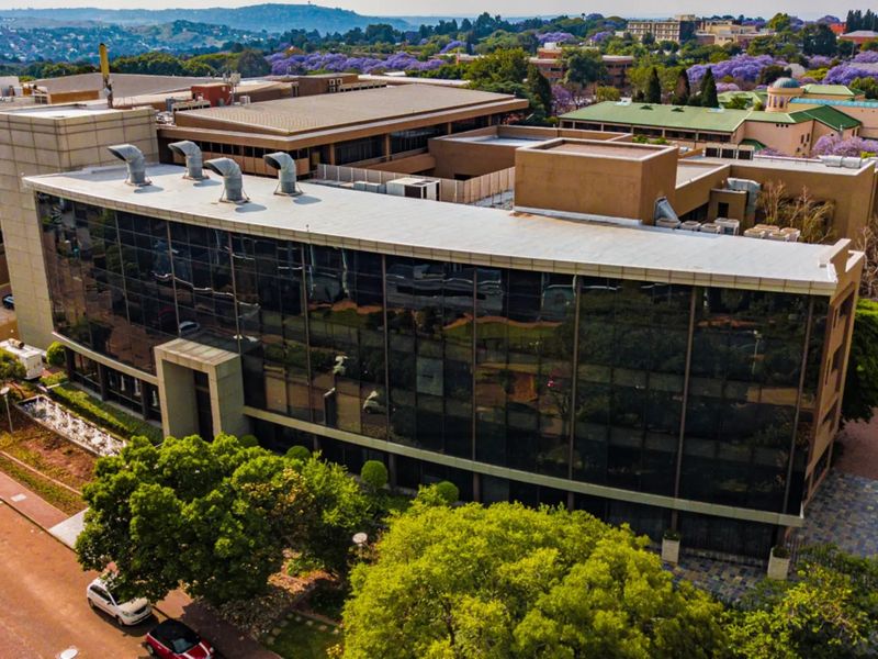 Aerial view of a modern commercial office building featuring extensive glass curtain walling, flat roof infrastructure, and surrounding landscaped grounds.