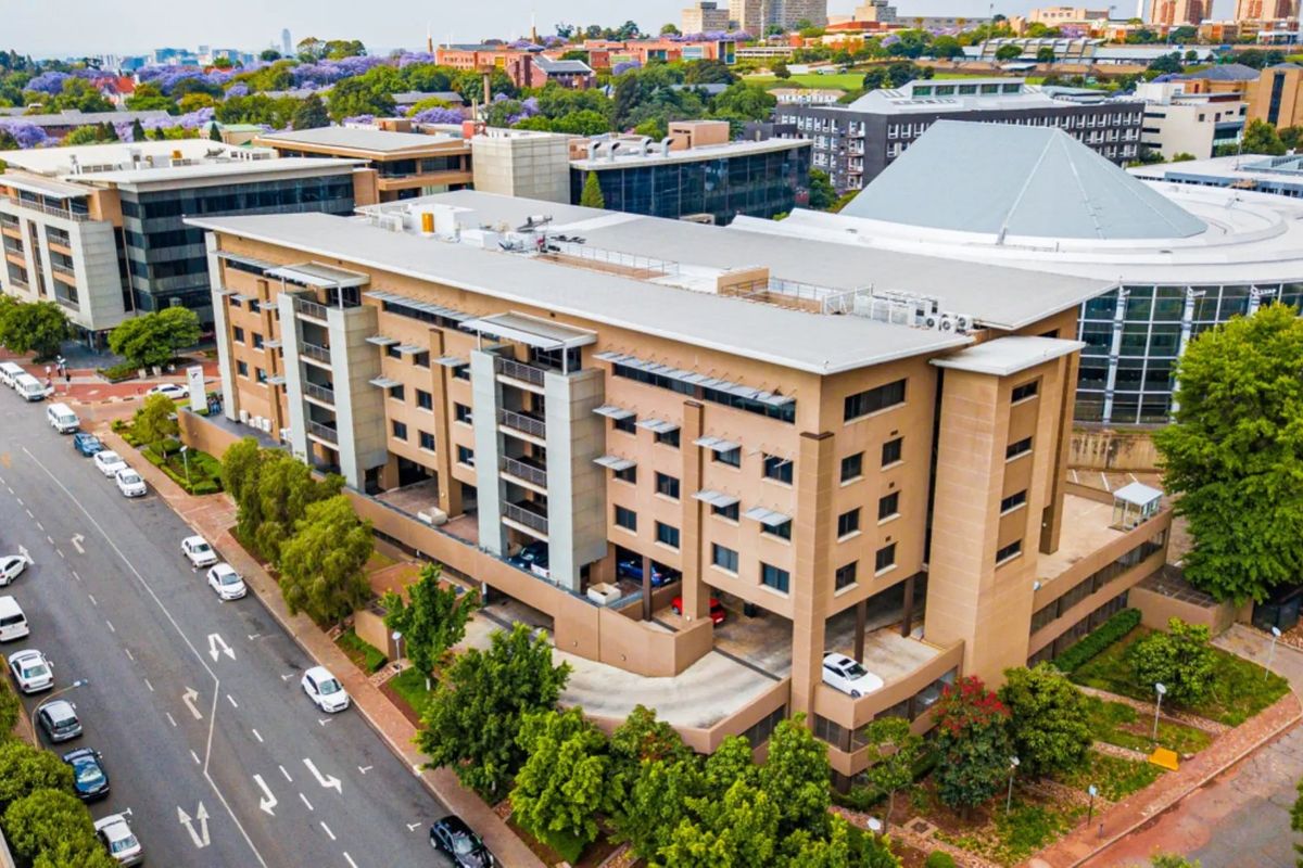 Aerial view of a multi-story commercial office building featuring a flat roof, external balconies, and integrated covered parking facilities in an urban setting.