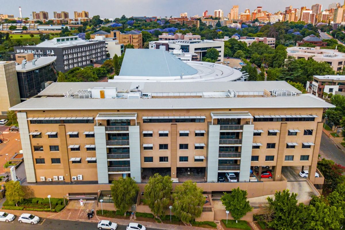 Aerial view of a multi-story commercial office building featuring a metal roof, integrated HVAC systems, and ground-level parking access within an urban setting.