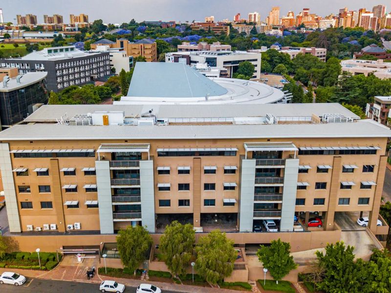 Aerial view of a multi-story commercial office building featuring a metal roof, integrated HVAC systems, and ground-level parking access within an urban setting.