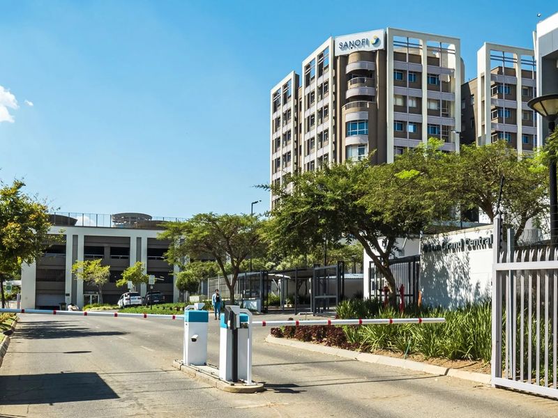 View of the secure entrance to a commercial office complex featuring a boom gate, paved driveway, and multi-story building with parking facilities.