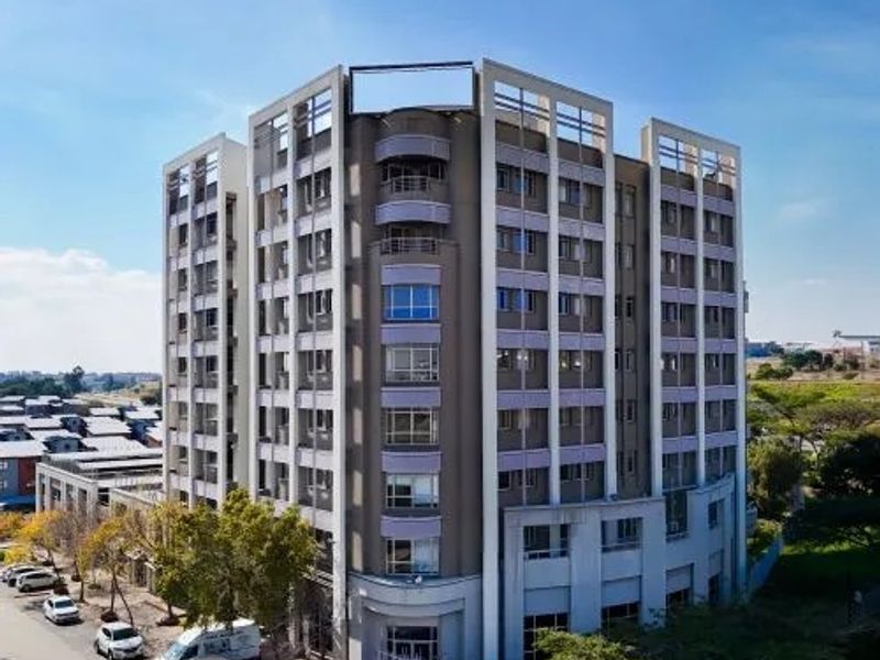 Aerial view of a multi-story commercial office building featuring a modern facade, integrated balconies, and an adjacent paved parking area.