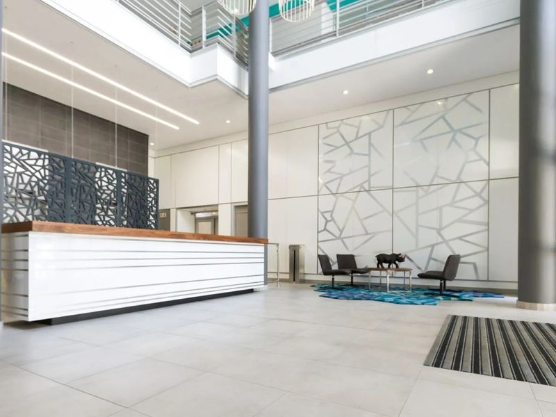 Modern commercial building entrance featuring a double-volume lobby, reception desk, structural columns, and contemporary decorative wall finishes with high-quality tiled flooring.