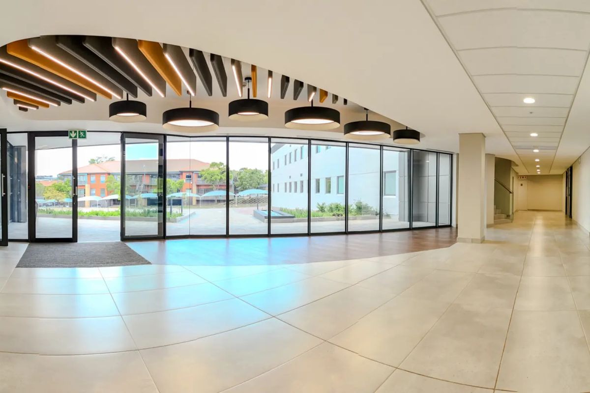 Spacious modern commercial entrance lobby featuring floor-to-ceiling glass walls, decorative acoustic ceiling baffles, and high-quality tiled flooring with a bright, open-plan layout.