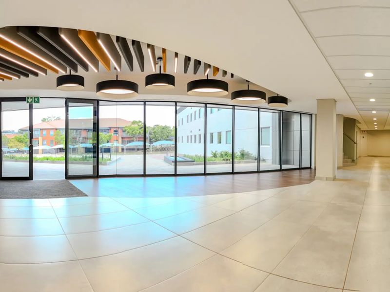 Spacious modern commercial entrance lobby featuring floor-to-ceiling glass walls, decorative acoustic ceiling baffles, and high-quality tiled flooring with a bright, open-plan layout.