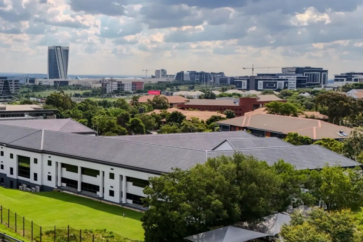 Aerial view of a commercial office complex featuring a tiled roof building, landscaped grounds, and a paved parking area with shade cloth carports.