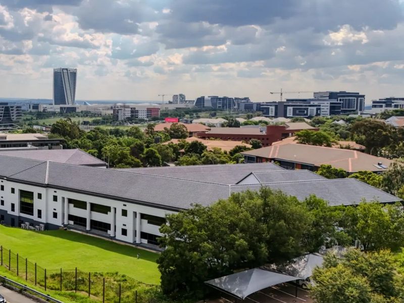 Aerial view of a commercial office complex featuring a tiled roof building, landscaped grounds, and a paved parking area with shade cloth carports.
