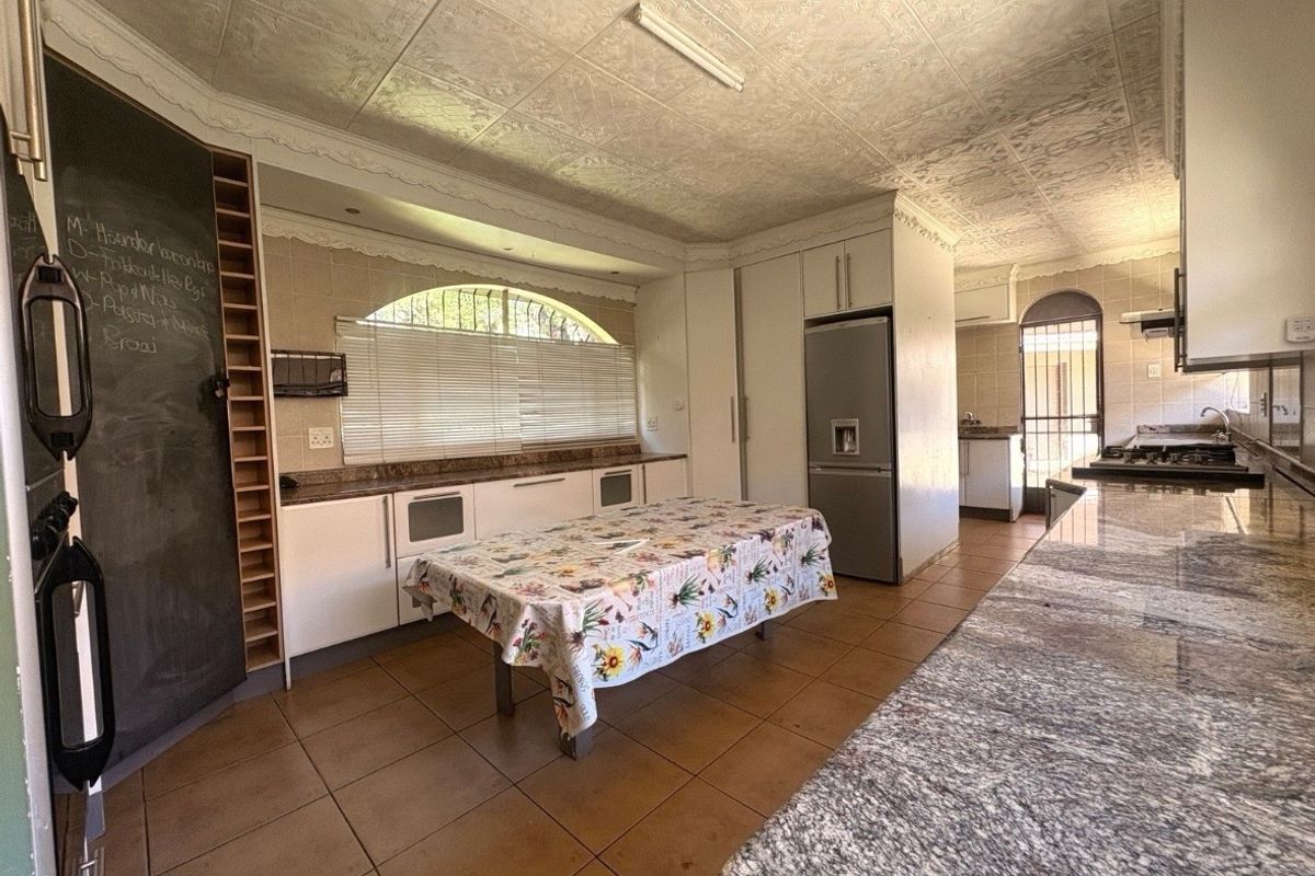 Spacious kitchen featuring granite countertops, ample built-in cabinetry, a gas hob with extractor, and tiled flooring, leading to a secondary prep area.