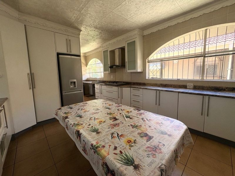 A functional kitchen featuring white built-in cabinetry, granite countertops, a gas hob with extractor fan, and distinctive arched windows with security bars.