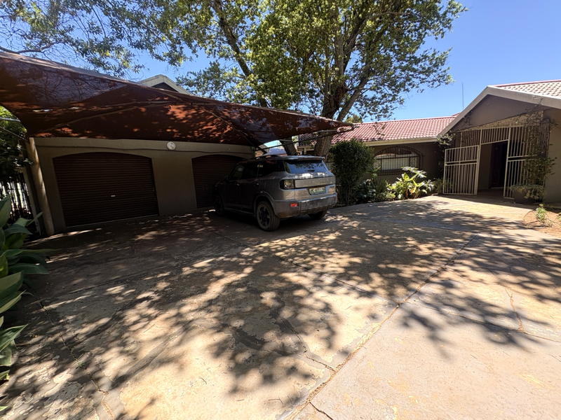 Front exterior view featuring a paved driveway, double garage with shade cloth carport, and secure gated entrance.