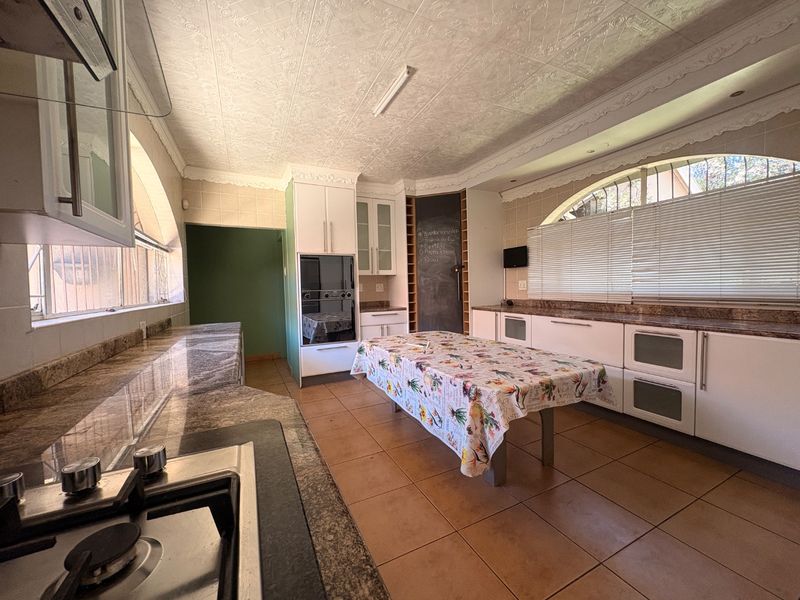 Spacious kitchen featuring granite countertops, built-in oven, gas hob, and decorative ceiling tiles, offering ample workspace and storage in a traditional layout.