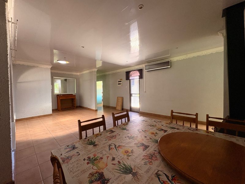 Spacious living area featuring tiled flooring, recessed lighting, and a wall-mounted air conditioning unit, offering a functional layout with potential for modern updates.