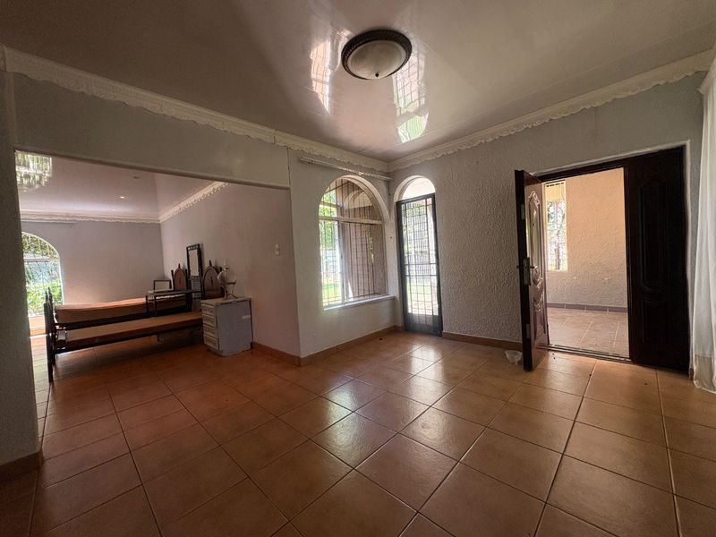 Spacious living area featuring tiled flooring, arched windows with security bars, and decorative ceiling cornices, offering direct access to an outdoor patio.