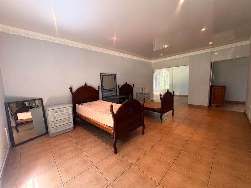 Spacious bedroom featuring ceramic floor tiles, recessed downlighting, and decorative ceiling cornicing, offering a neutral canvas for potential interior updates.