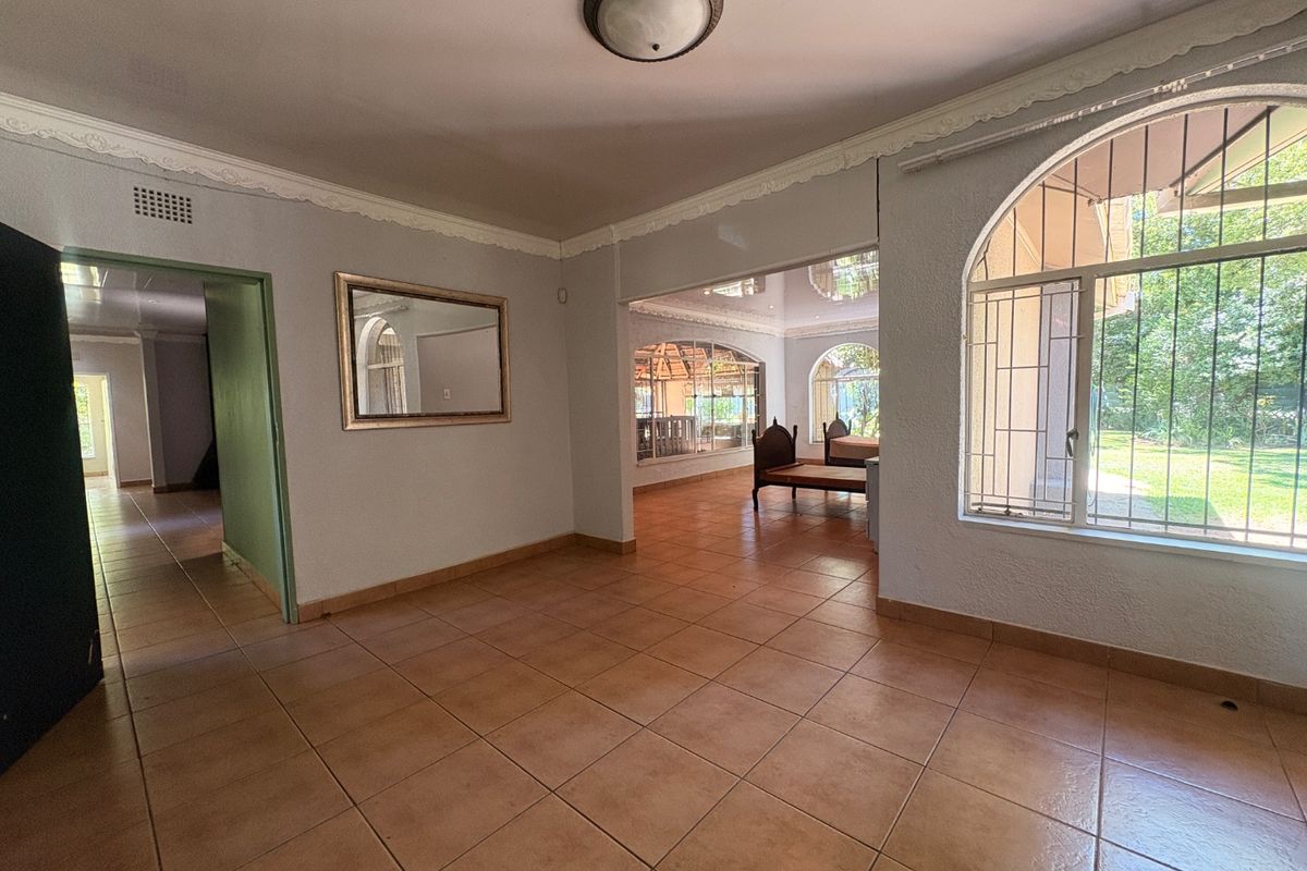 Spacious living area featuring ceramic floor tiles, decorative ceiling cornices, and large arched windows with security bars, offering a bright and open layout.