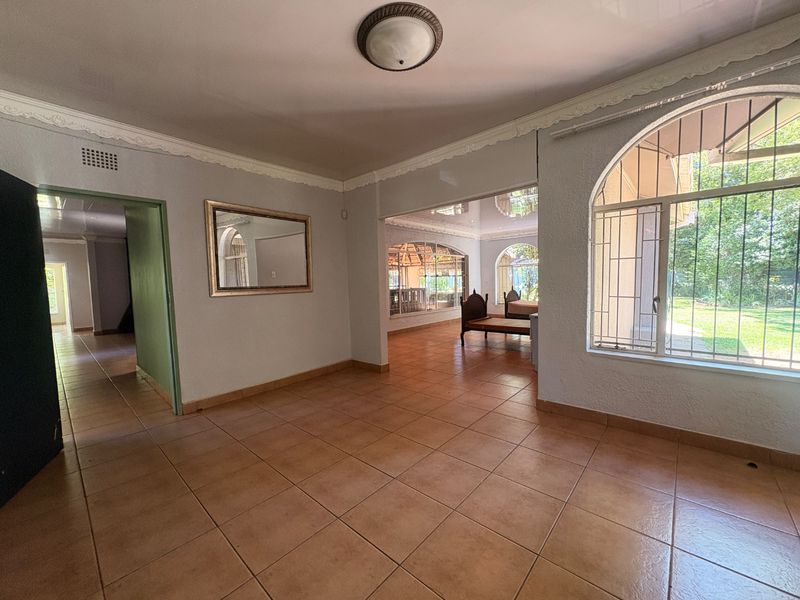 Spacious living area featuring ceramic floor tiles, decorative ceiling cornices, and large arched windows with security bars, offering a bright and open layout.