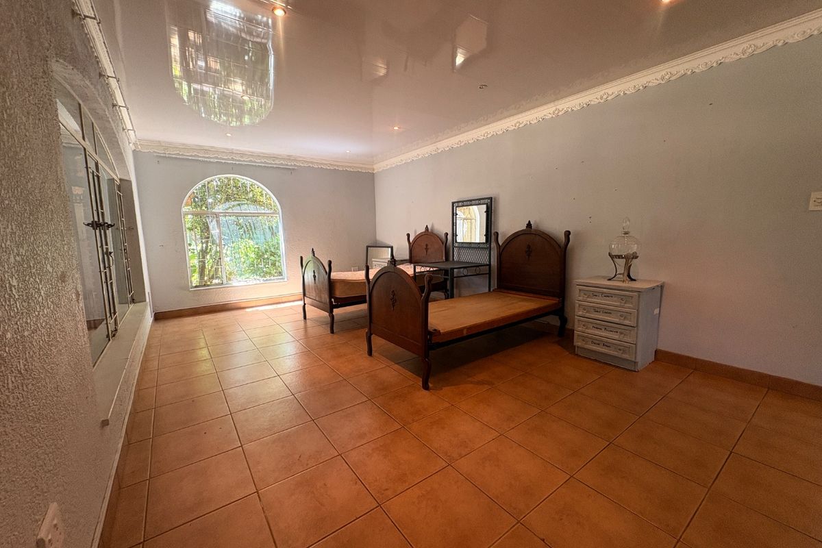 Spacious bedroom featuring tiled flooring, a glossy ceiling with decorative cornice, and an arched window with security bars.