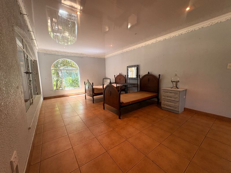 Spacious bedroom featuring tiled flooring, a glossy ceiling with decorative cornice, and an arched window with security bars.