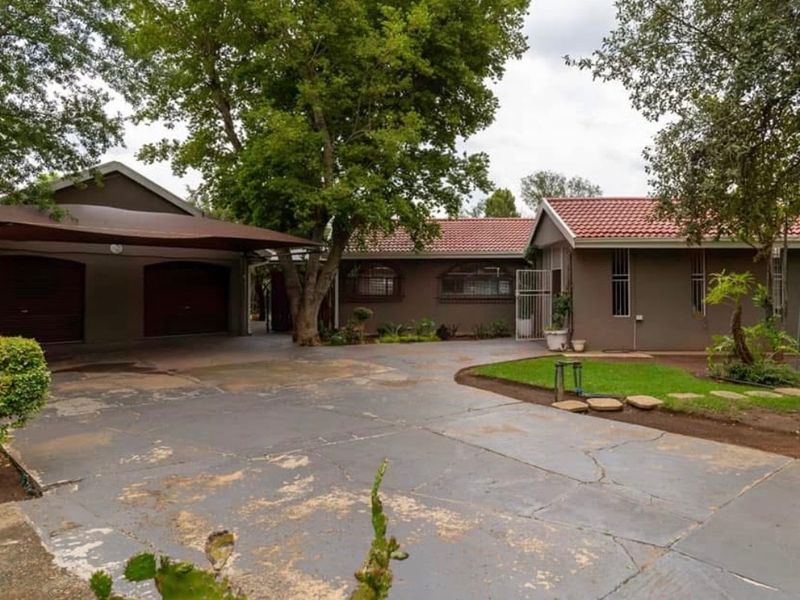 Front exterior view of the property featuring a paved driveway, carport, garage, and established garden area with tiled roof architecture.