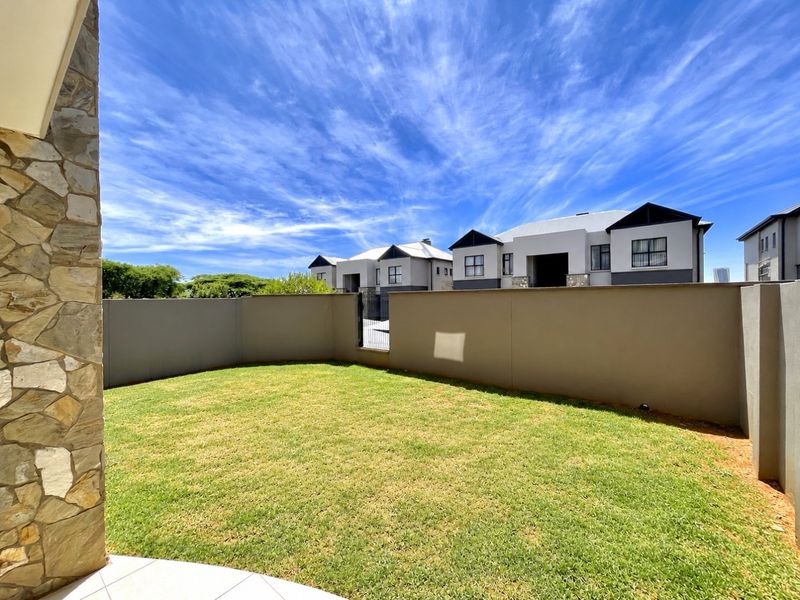 A private rear garden featuring a well-maintained lawn, enclosed by solid boundary walls and stone-clad architectural detailing.