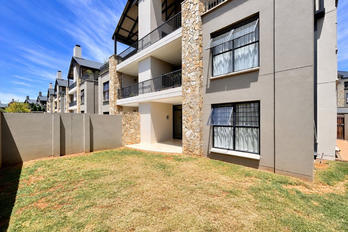Rear view of a modern apartment building featuring stone-clad accents, a private patio, and a small garden area with metal balcony railings.