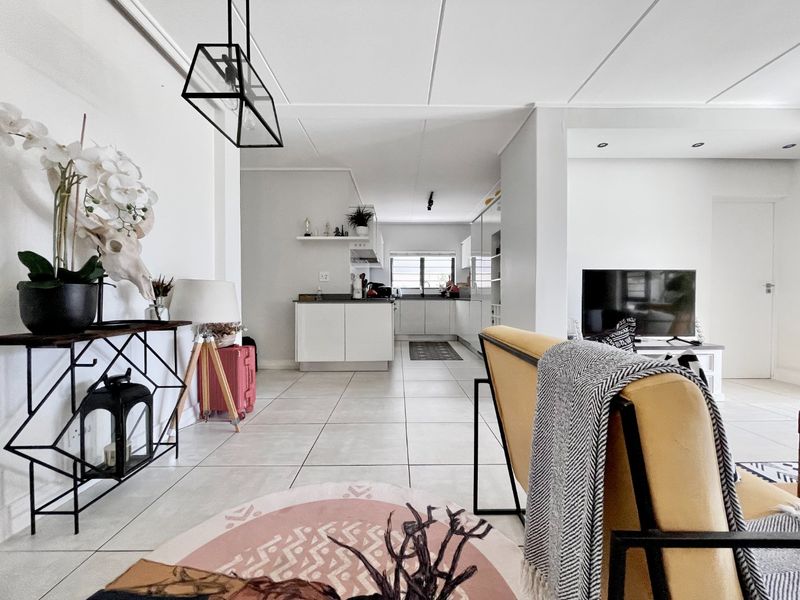 A bright open-plan living and kitchen area featuring modern tiled flooring, clean white cabinetry, and contemporary lighting fixtures throughout the space.