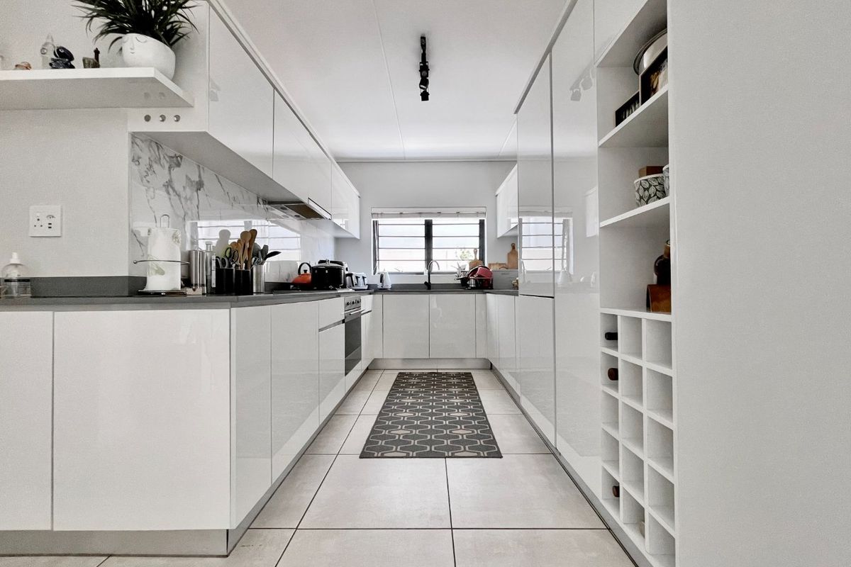 Modern galley-style kitchen featuring high-gloss white cabinetry, integrated oven, marble-look splashback, and dedicated wine storage with sleek tiled flooring.