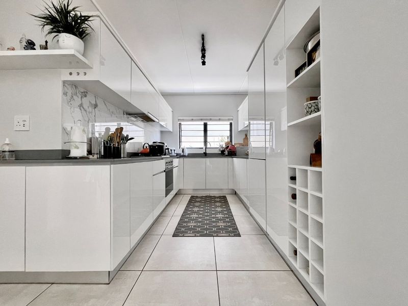 Modern galley-style kitchen featuring high-gloss white cabinetry, integrated oven, marble-look splashback, and dedicated wine storage with sleek tiled flooring.