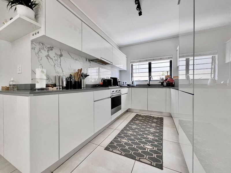 Modern kitchen featuring sleek white cabinetry, marble-look splashback, stone countertops, integrated oven, and high-quality tiled flooring.