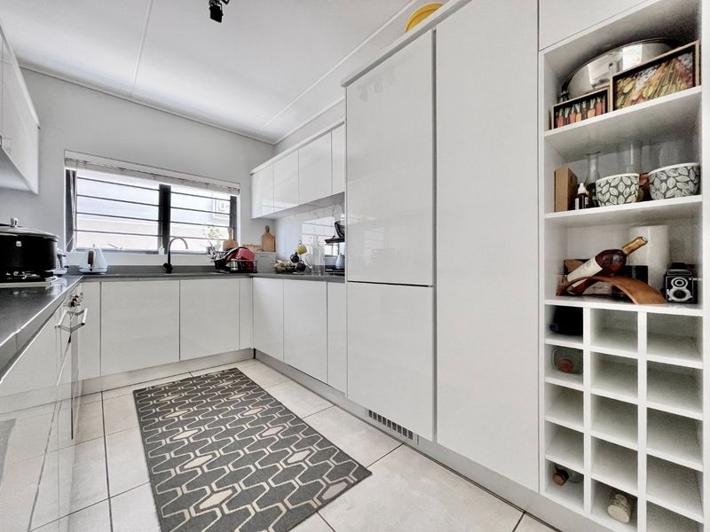 Modern kitchen featuring sleek white cabinetry, integrated appliances, stone countertops, and a dedicated wine rack, offering a clean and functional culinary space.