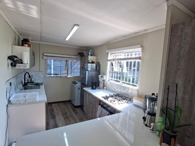 Functional kitchen featuring quartz countertops, gas hob, built-in oven, and ample cabinetry, offering a practical layout with natural light from dual windows.