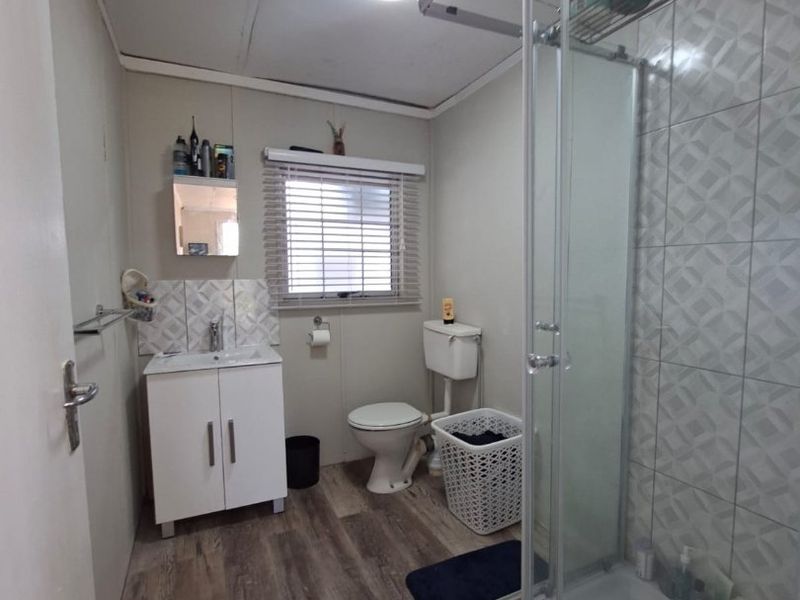 A functional bathroom featuring a glass-enclosed shower, vanity cabinet with basin, and toilet, finished with wood-look laminate flooring and tiled shower walls.